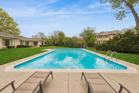 a view of an swimming pool with lawn chairs and large trees