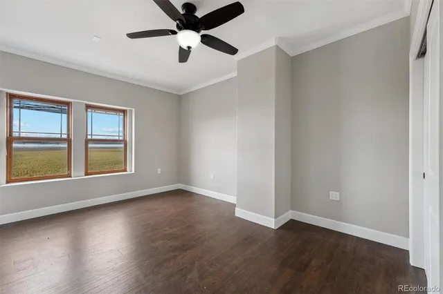 an empty room with wooden floor chandelier fan and windows