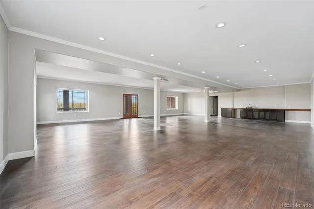 a view of empty room with wooden floor and kitchen