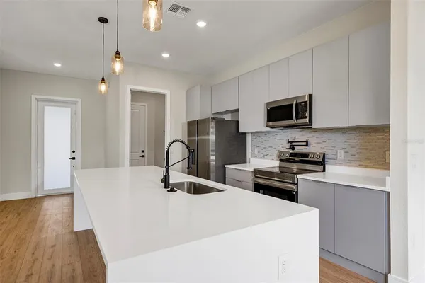 a kitchen with stainless steel appliances a stove top oven a sink a refrigerator white cabinets and wooden floor