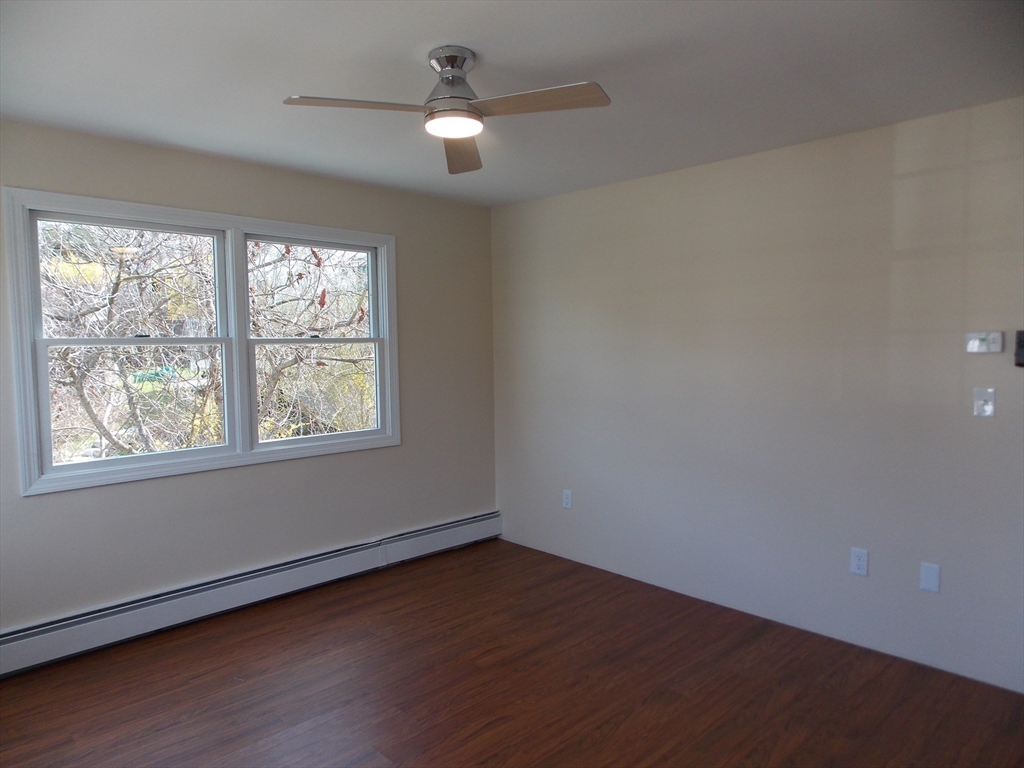 196 Main Street, Unit A Rockport, MA 01966 - Photo 18 of 36 an empty room with wooden floor chandelier fan and windows