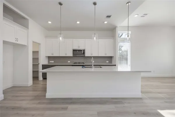 a large kitchen with stainless steel appliances granite countertop a stove a sink a refrigerator and white cabinets with wooden floor