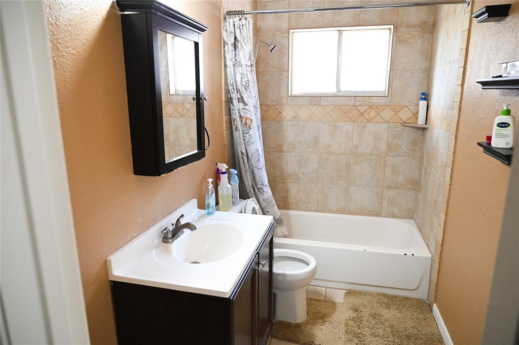 1352 Simpson Drive Hurst, TX 76053 - Photo 12 of 40 Bathroom featuring a single vanity with a white countertop and dark wood-finish cabinetry, a mirror-front medicine cabinet, a tiled shower/tub combination with a decorative accent band, and a window