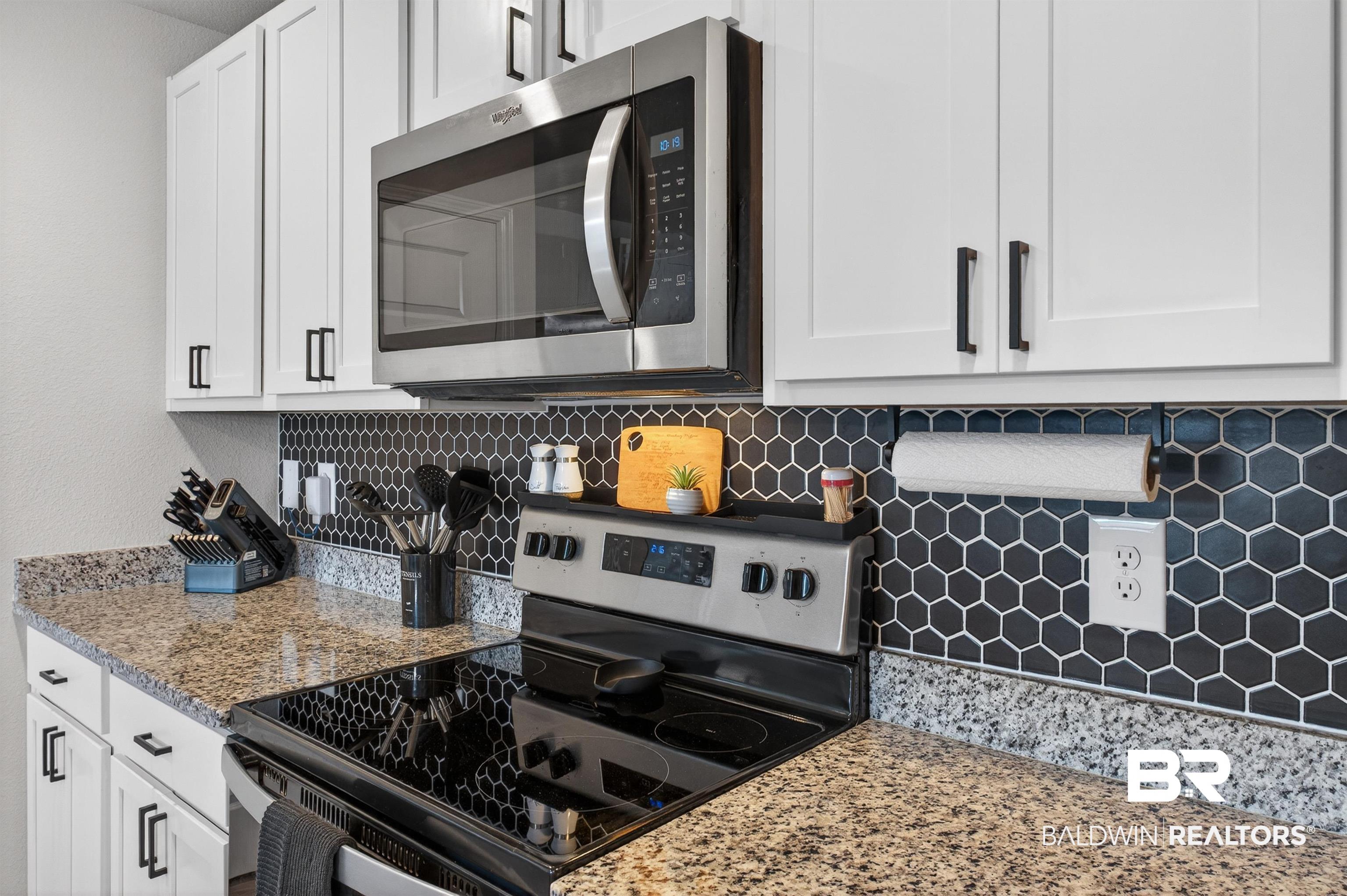 3213 Camino Real Loop Lillian, AL 36549 - Photo 32 of 61 Modern kitchen featuring white cabinetry with black hardware, granite-style countertops, a black hexagonal tile backsplash, a stainless steel over-the-range microwave, and a black electric range with a glass cooktop