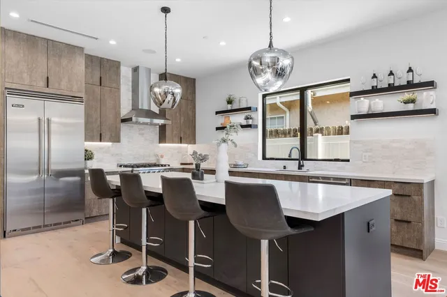 a large white kitchen with a large island oven a stove a sink a refrigerator and a dining table