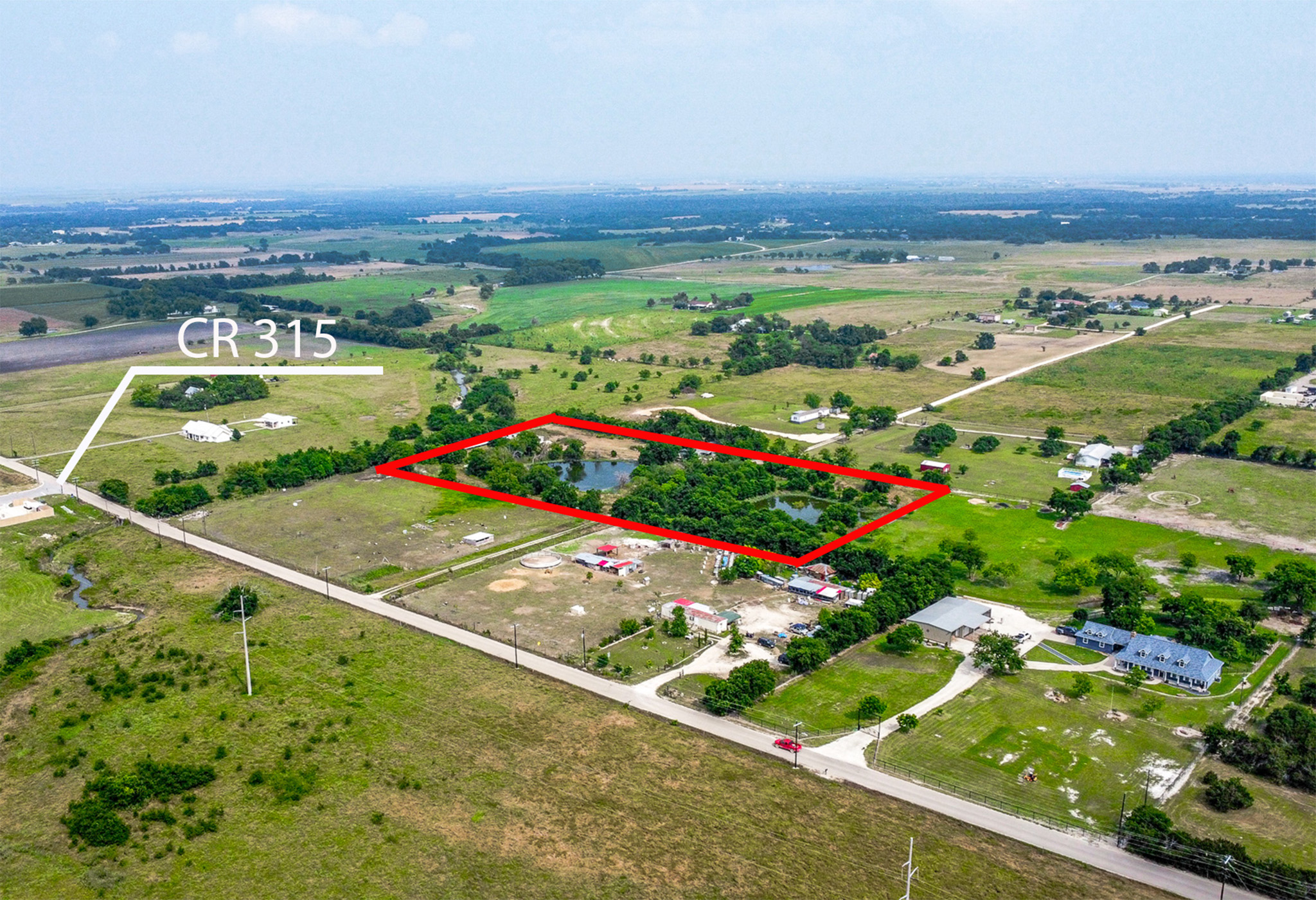 Expansive rural property featuring a natural pond, mature trees, open grasslands, and a perimeter of fencing