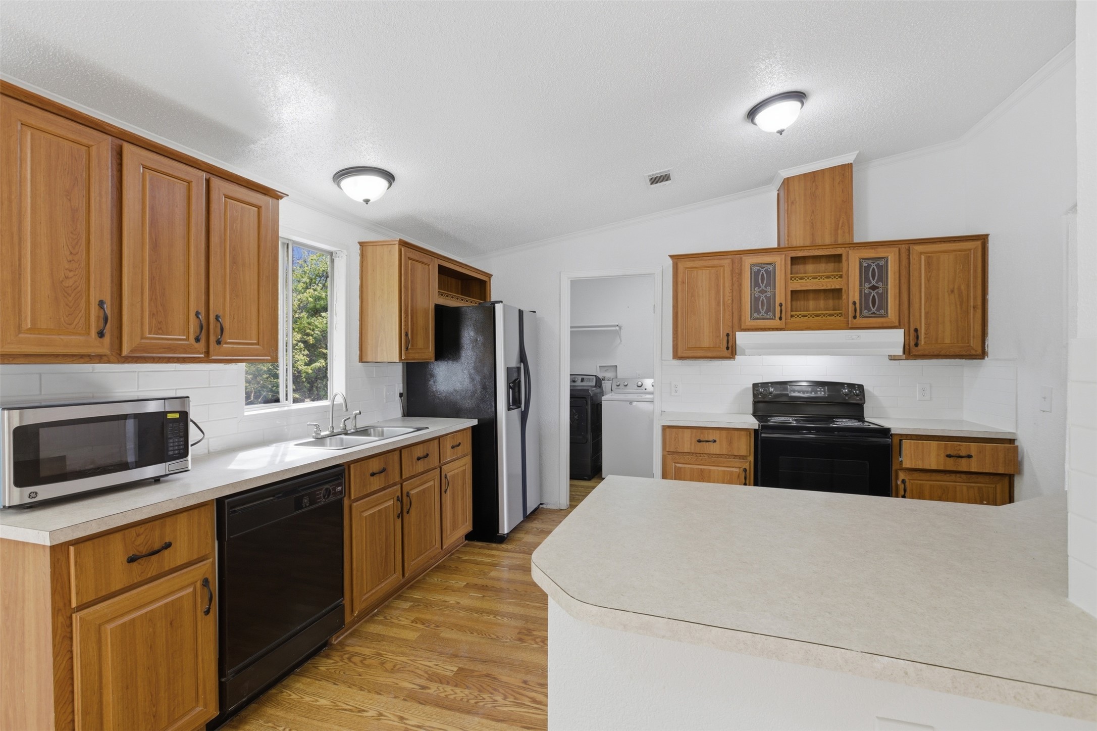 376 Rae Lane, Unit A Jarrell, TX 76537 - Photo 12 of 31 Open-concept kitchen featuring wood-finish cabinetry, light-toned countertops, white subway tile backsplash, and wood-finish flooring