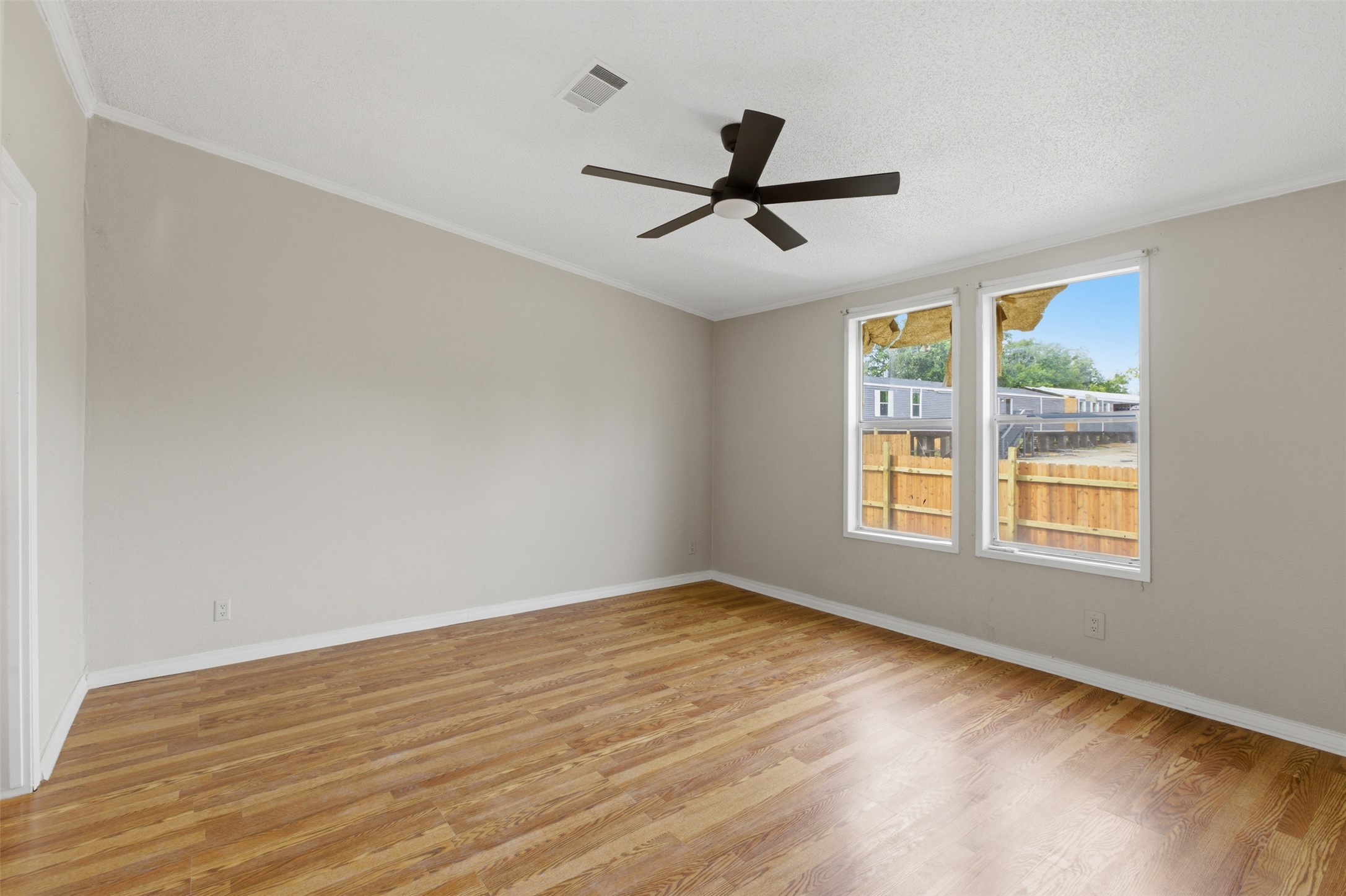 376 Rae Lane, Unit A Jarrell, TX 76537 - Photo 13 of 31 Spacious room featuring wood-finish flooring, light neutral wall tones, two white-framed windows, a dark ceiling fan, and white baseboards