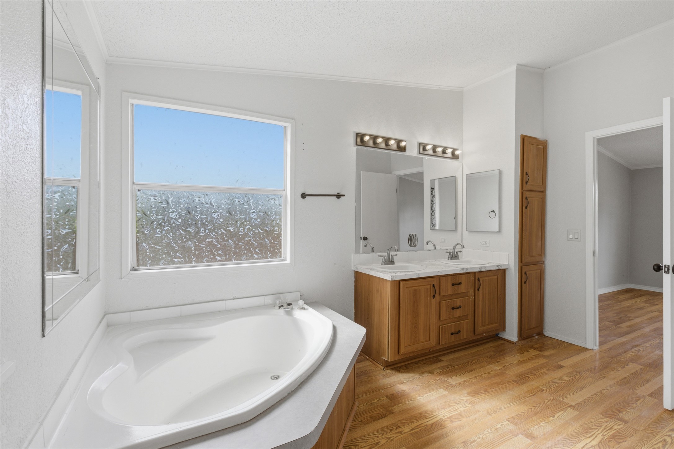376 Rae Lane, Unit A Jarrell, TX 76537 - Photo 14 of 31 Bathroom featuring a corner soaking tub with a frosted window, wood-finish flooring, and a double vanity with light wood cabinetry and dual sinks