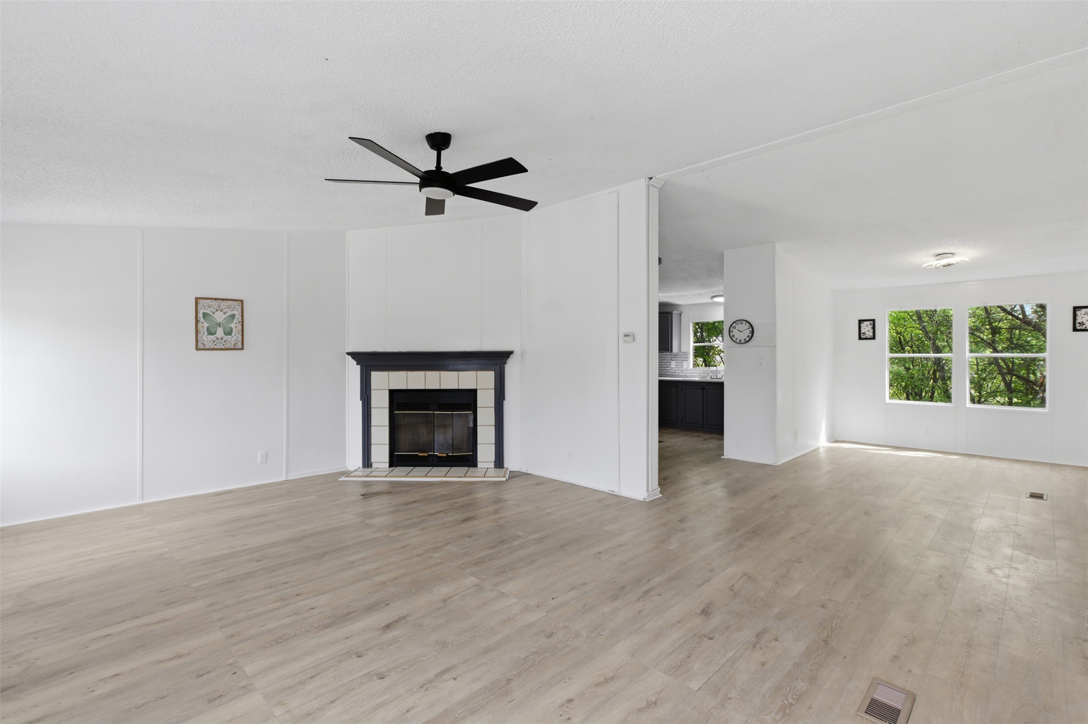 376 Rae Lane, Unit A Jarrell, TX 76537 - Photo 24 of 31 Living area featuring light wood-finish flooring, a black ceiling fan, and a fireplace with a white tile surround and dark mantel