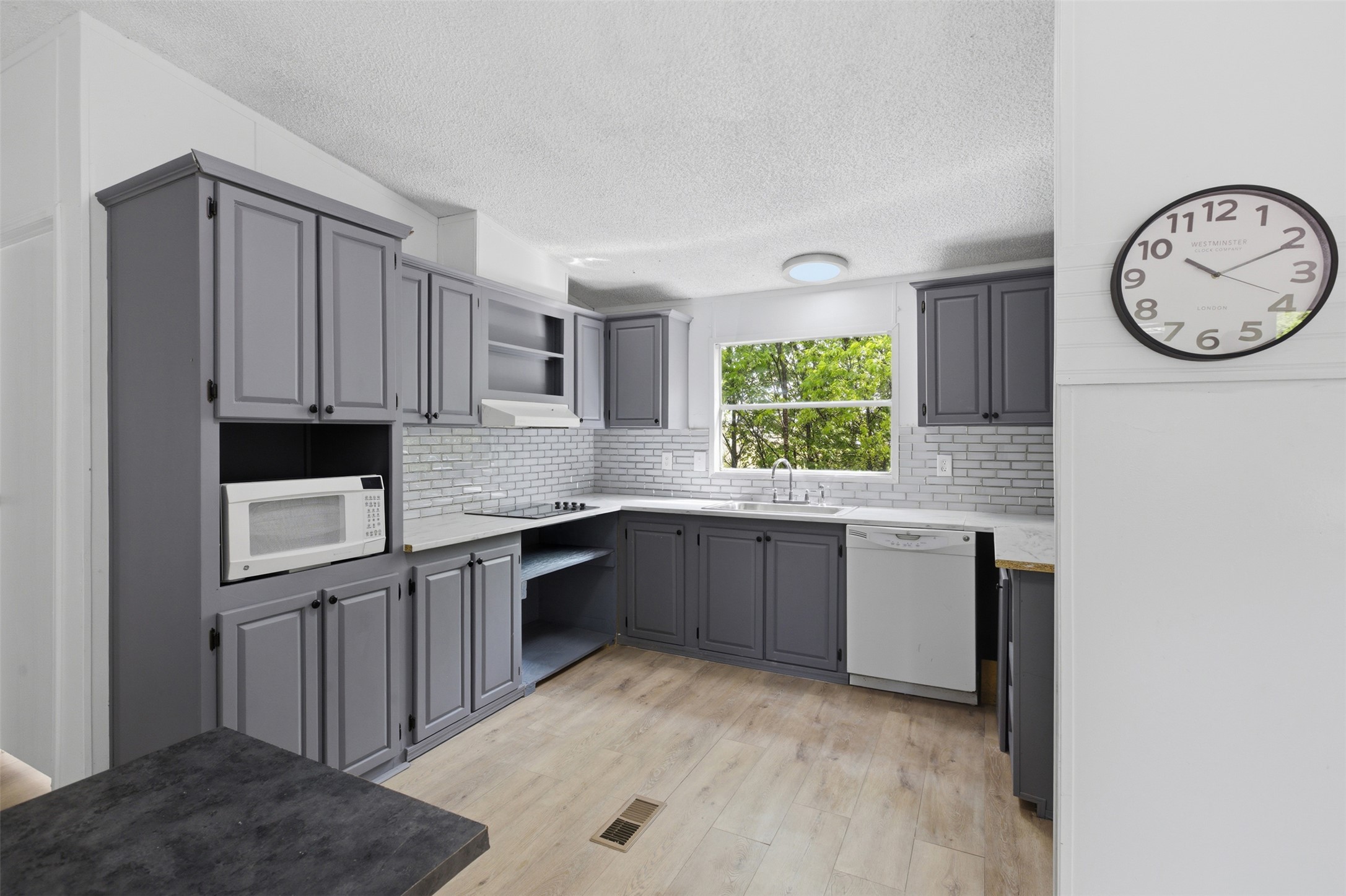 376 Rae Lane, Unit A Jarrell, TX 76537 - Photo 26 of 31 Kitchen featuring grey cabinetry, light wood-finish flooring, a white subway tile backsplash, and light-colored countertops