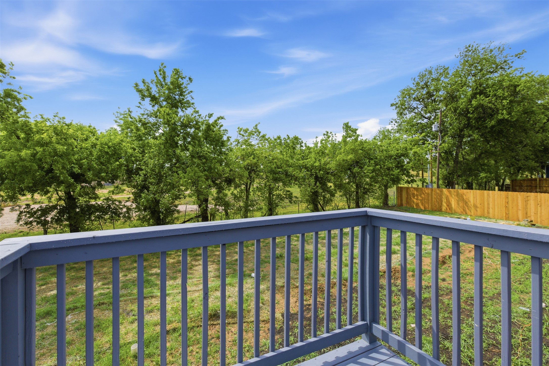 376 Rae Lane, Unit A Jarrell, TX 76537 - Photo 30 of 31 Outdoor deck with painted railing overlooking a spacious grassy area, perimeter trees, and a wooden privacy fence