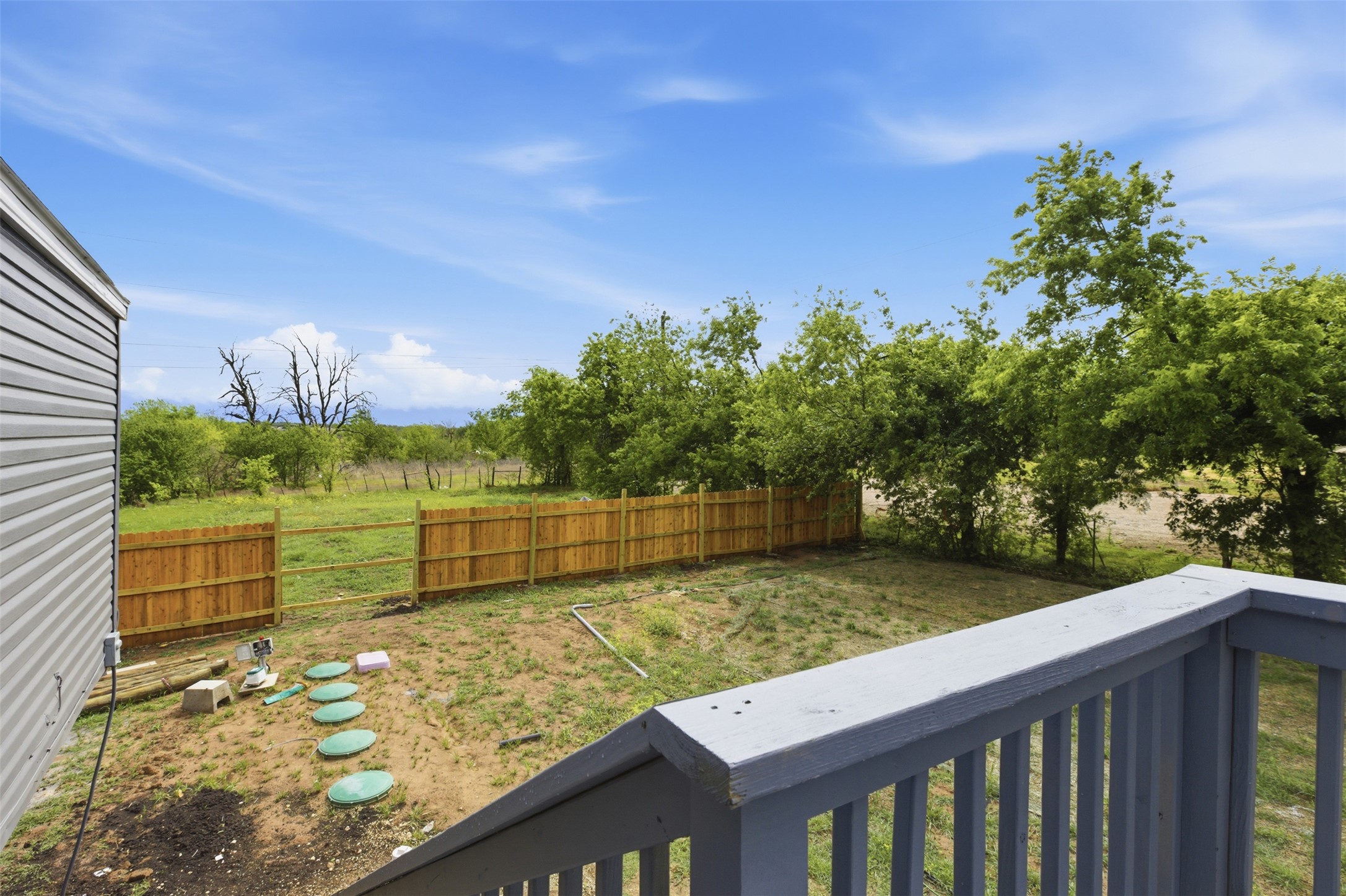 376 Rae Lane, Unit A Jarrell, TX 76537 - Photo 31 of 31 Expansive rear yard featuring a wood privacy fence, mature trees, and a gray-painted deck with railings