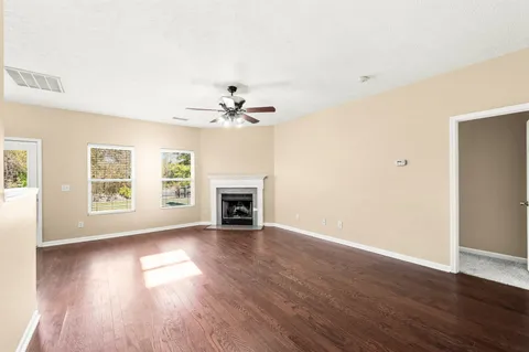 a view of an empty room with wooden floor fireplace and a window