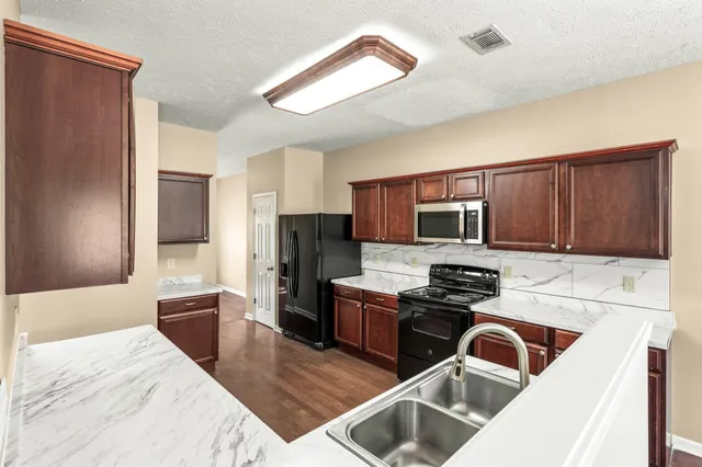 a kitchen with stainless steel appliances granite countertop wooden cabinets a stove top oven a sink and dishwasher with wooden floor