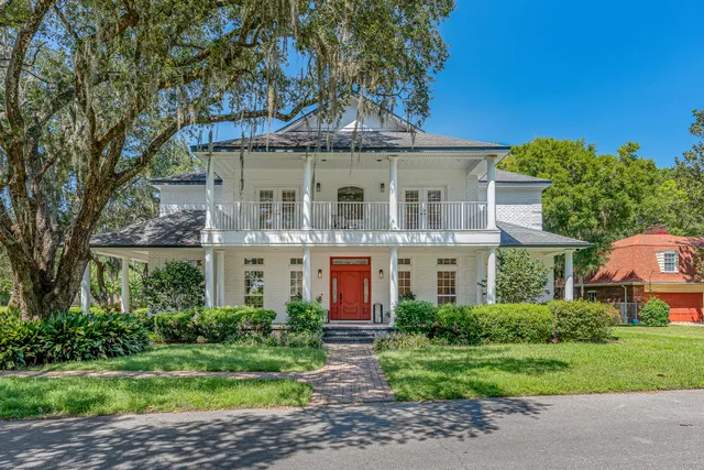 a view of a big yard in front of a brick house with plants and large trees