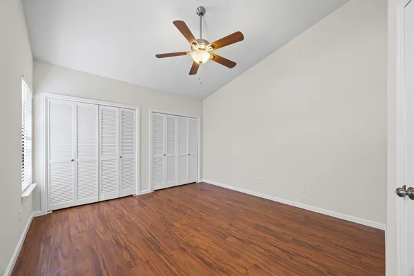 a view of an empty room with wooden floor and a ceiling fan