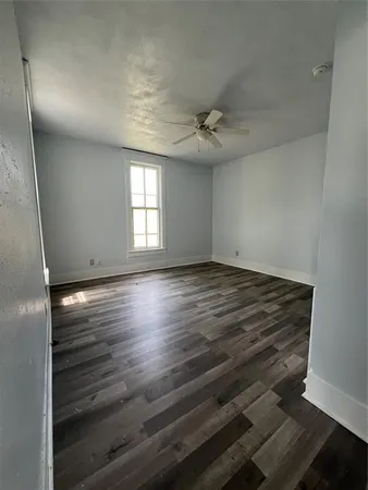 an empty room with wooden floor and windows with curtains