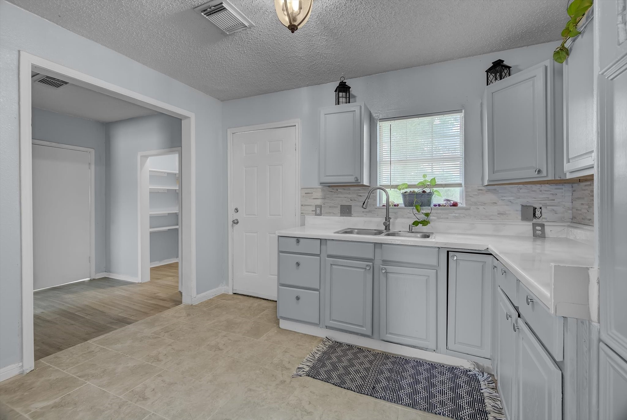 418 Azalea Street Lake Jackson, TX 77566 - Photo 2 of 34 This kitchen features light gray cabinets, a sleek light countertop, and a neutral tile floor. It includes a window above the sink for natural light, modern fixtures, and adjacent access to a room with built-in shelving and vinyl flooring.