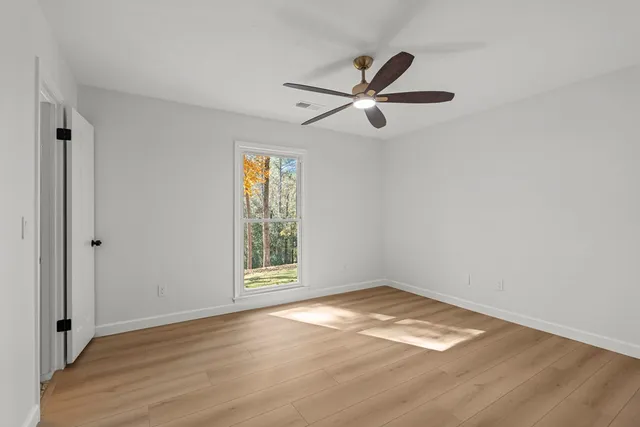 an empty room with wooden floor fan and windows