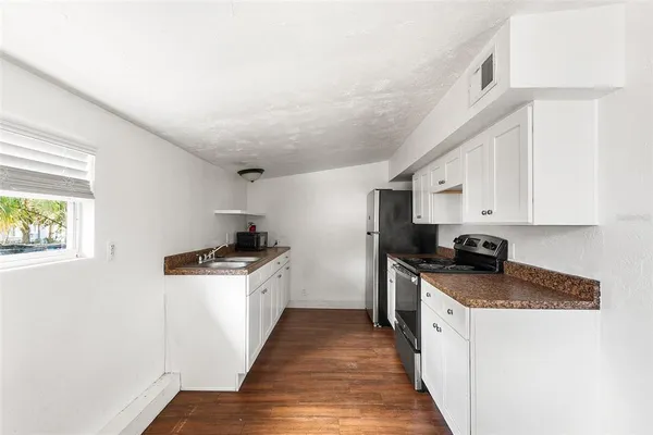 a kitchen with granite countertop a sink a stove top oven and cabinetry