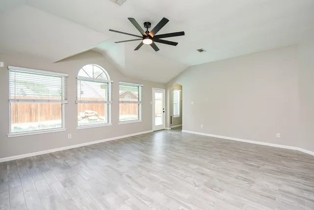 an empty room with wooden floor fan and windows