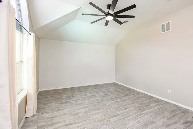 an empty room with wooden floor fan and windows