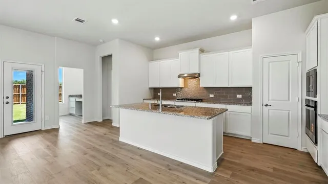 a kitchen with stainless steel appliances granite countertop a refrigerator a sink dishwasher and white cabinets with wooden floor