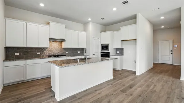 a large kitchen with stainless steel appliances granite countertop a stove a sink and white cabinets