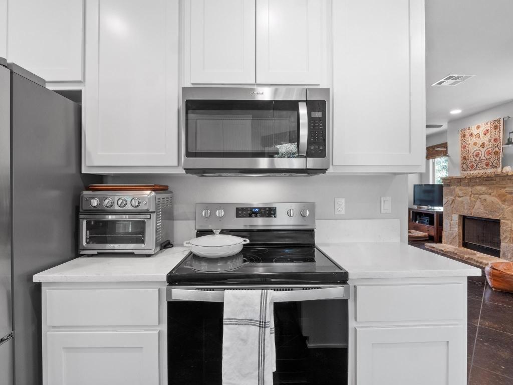 10103 Twin Lake Loop Dripping Springs, TX 78620 - Photo 16 of 32 Kitchen with stainless steel appliances, light countertops, white cabinets, and a fireplace