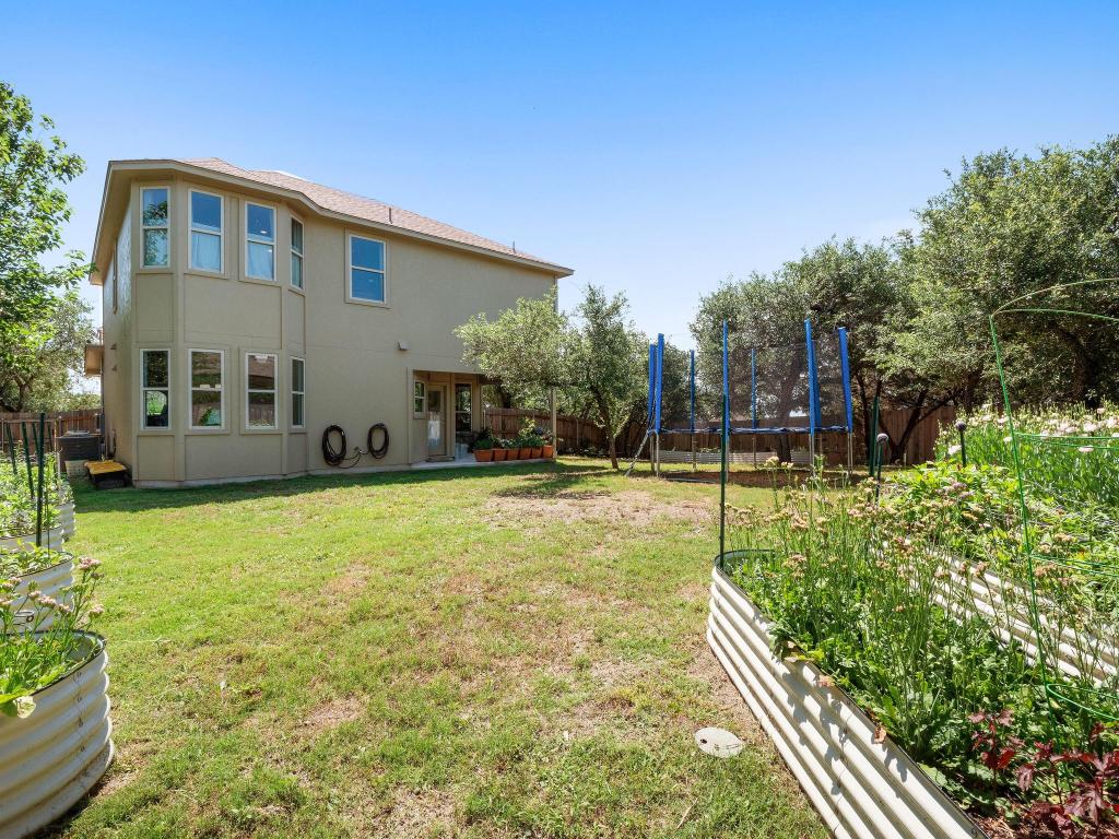 10103 Twin Lake Loop Dripping Springs, TX 78620 - Photo 31 of 32 Rear view of property with a trampoline, a vegetable garden, and stucco siding