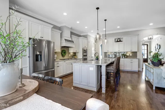 a kitchen with stainless steel appliances granite countertop a stove top oven a sink dishwasher a refrigerator and a dining table with wooden floor