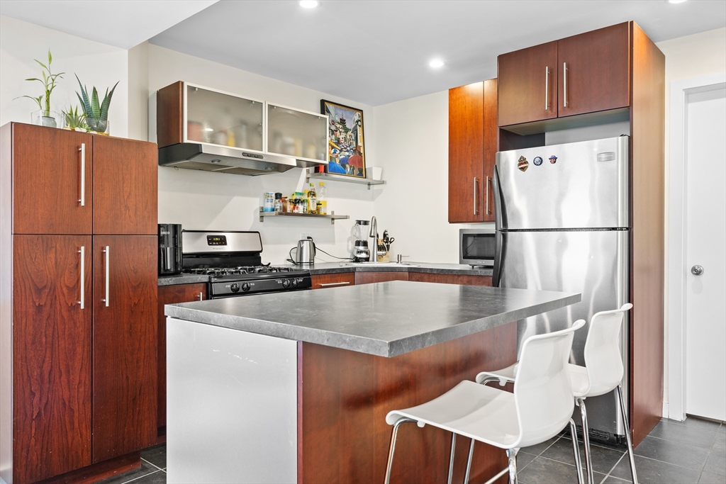 62 Grampian Way, Unit STUDIO Boston, MA 02125 - Photo 9 of 25 a kitchen with stainless steel appliances granite countertop a refrigerator a stove and a sink with wooden floor