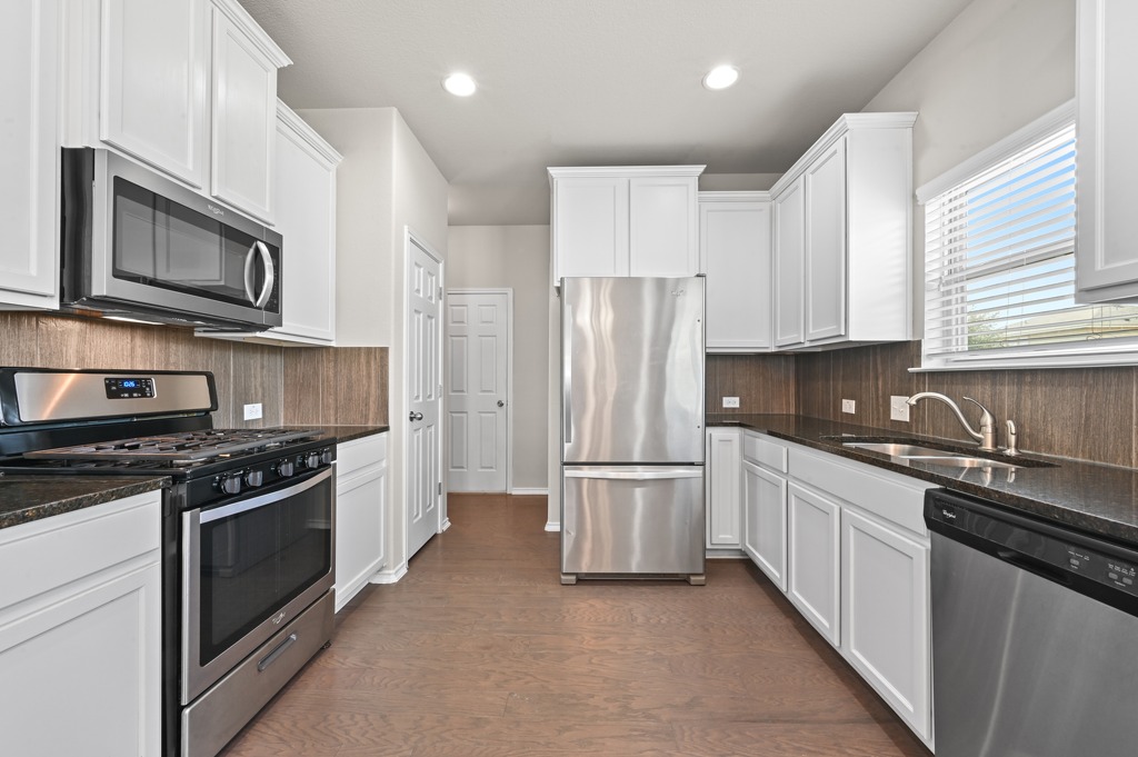 209 Noddy Road Buda, TX 78610 - Photo 11 of 27 Gleaming stone countertops and stainless steel appliances complement classic recessed lighting and wood floors.