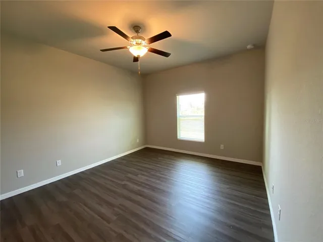 an empty room with wooden floor chandelier fan and windows