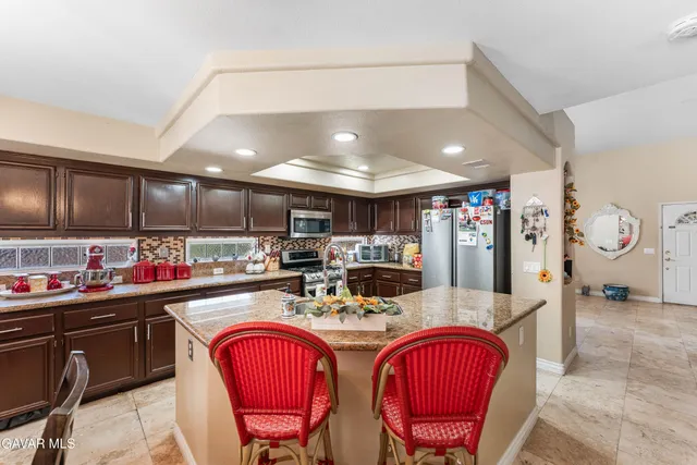 a kitchen with stainless steel appliances granite countertop a sink a stove a refrigerator cabinets and chairs