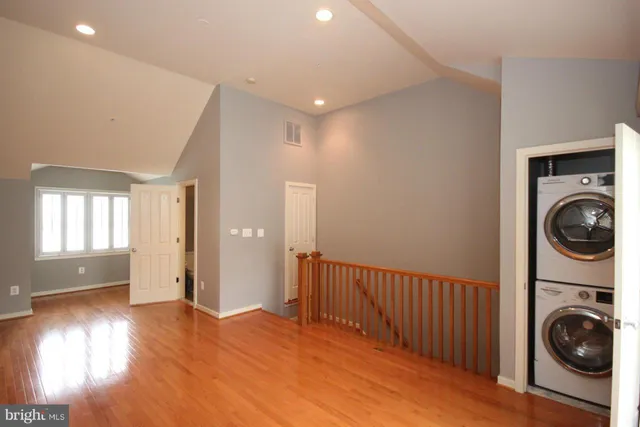 a view of a hallway to an empty room with wooden floor and a window