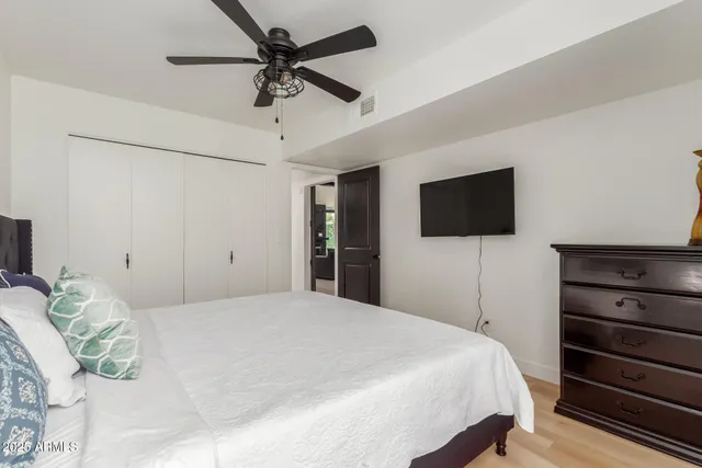 a bedroom with a bed a flat tv screen and a ceiling fan