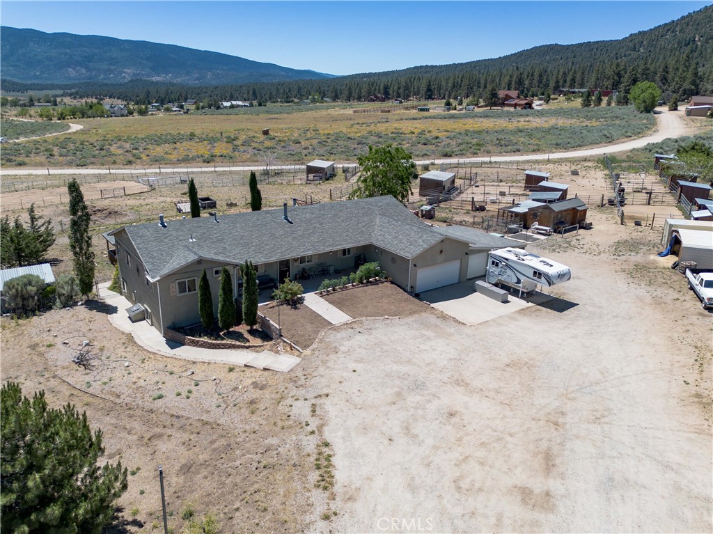 10960 Steinhoff Road Frazier Park, CA 93225 - Photo 2 of 46 A higher aerial perspective capturing the side and rear profile of the home, highlighting the transition from the residential driveway to the open pastures, equestrian areas, and scenic mountain range in the distance.