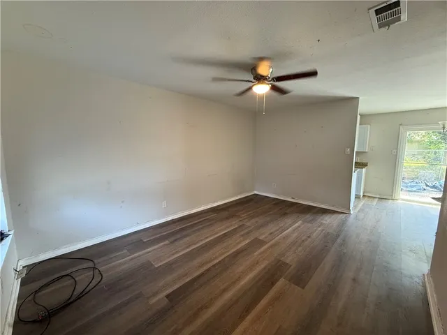 an empty room with wooden floor fan and windows