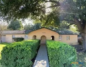 a view of a house with large trees and plants next to a road
