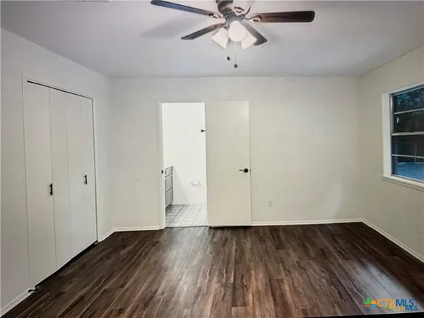 a view of an empty room with wooden floor and a ceiling fan