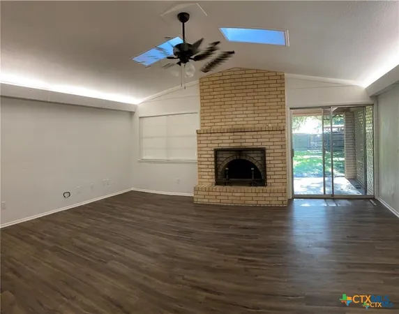 a view of an empty room with wooden floor a fireplace and a window