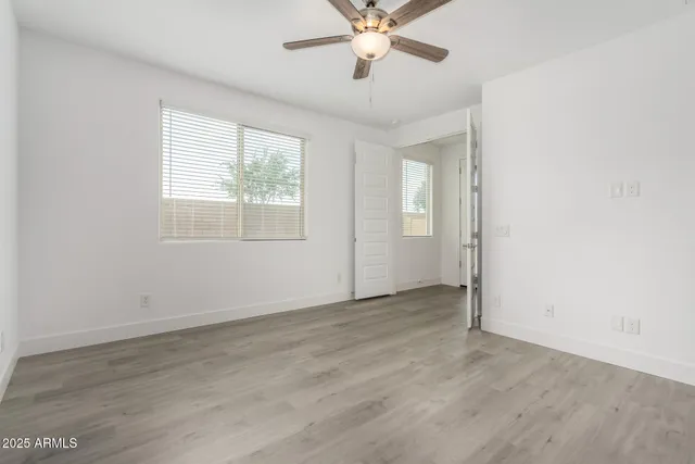 an empty room with wooden floor fan and windows