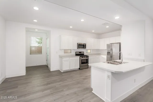 a kitchen with stainless steel appliances kitchen island granite countertop a refrigerator oven a sink dishwasher and white cabinets with wooden floor