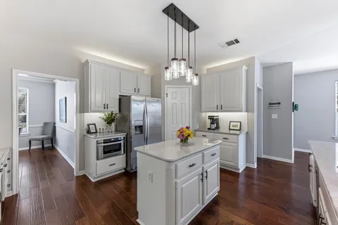 a kitchen with stainless steel appliances kitchen island granite countertop a refrigerator a oven a stove and a wooden floors