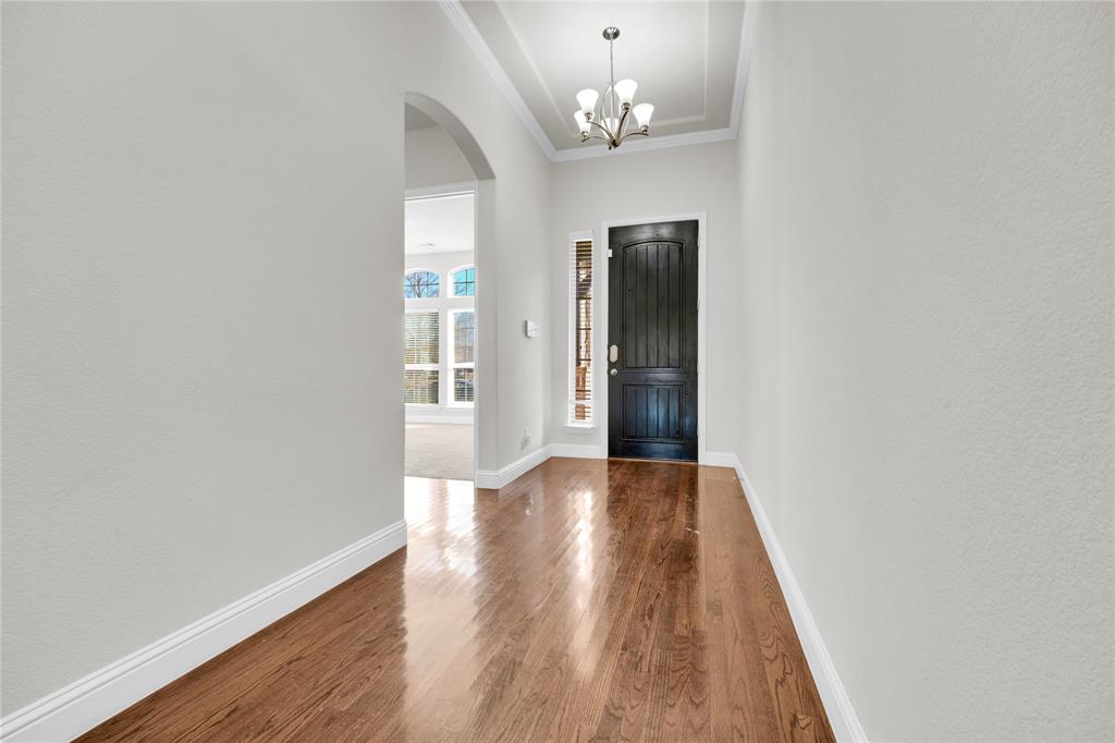 1011 Prairie Ridge Lane Arlington, TX 76005 - Photo 9 of 32 Entry hallway featuring wood-finish flooring, a dark paneled front door with a sidelight, a tray ceiling, and an arched doorway leading to another room with large windows