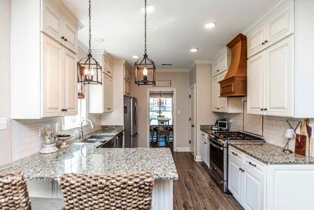 a kitchen with stainless steel appliances granite countertop a stove a sink a refrigerator white cabinets and wooden floor