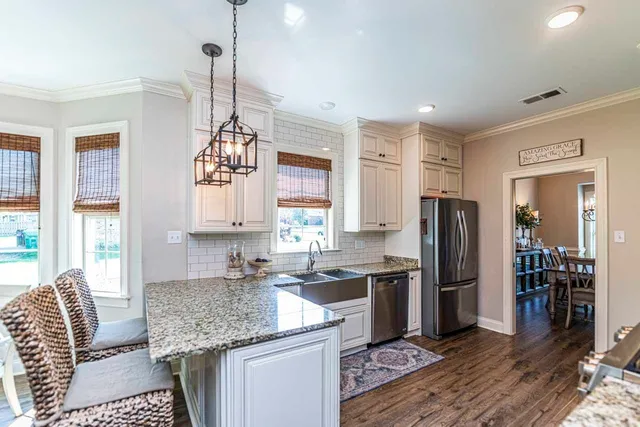 a kitchen with stainless steel appliances granite countertop a refrigerator a sink dishwasher a stove and white cabinets with wooden floor