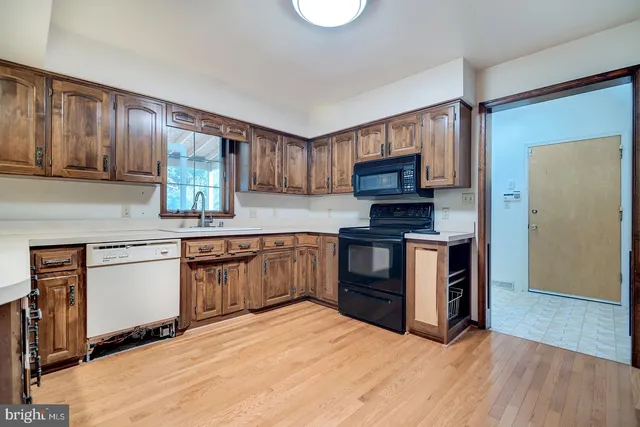 a view of an empty room with kitchen and wooden floor